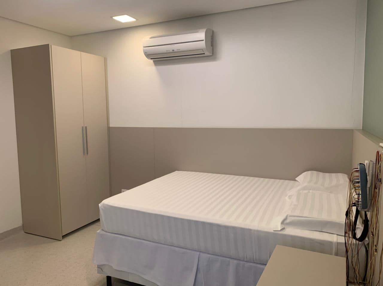 Suíte individual da clínica PolissonoNoLar, com cama queen, ar-condicionado e banheiro privativo